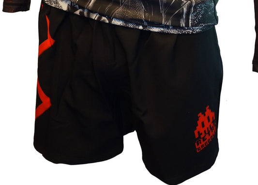 Someone wears Retro Grapplers Berserk Lightweight BJJ Shorts, featuring a red pixelated graphic and text on the right leg and a red angular design on the left, paired with a patterned black and white top. No Velcro closure.