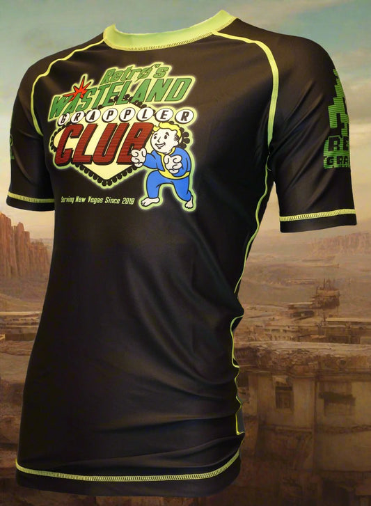 The Fallout Wasteland Grappler Rash Guard by Retro Grappler features black and neon green colors, the Wasteland Grappler Club logo with Vault Boy, cityscape details, and Serving New Vegas Since 2010. Limited edition for dedicated fans.