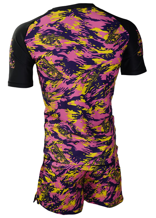 The Retro Grappler Thai Tiger Stripe Camo Kit features a back view of a short-sleeved rash guard and matching shorts, decorated with vibrant pink, yellow, and black abstract patterns plus cartoon fighter jets for a bold, unified look.