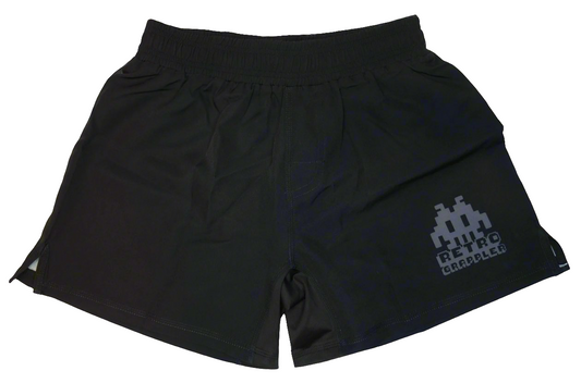 The Retro Grappler Simple Black Grappling Shorts are lightweight, feature an elastic waistband, small side slits, and no Velcro for comfort. A pixelated graphic and Retro Grappler text in light gray appear on the left leg.