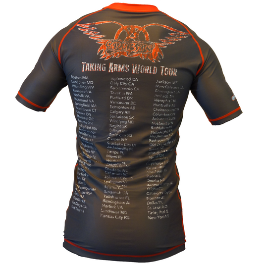 The Armbar Concert Tee Rash Guard by Retro Grappler is a black and orange BJJ rash guard with an eagle graphic on the back and “Taking Arms World Tour” plus cities and dates, styled like a jiu jitsu concert tour shirt.
