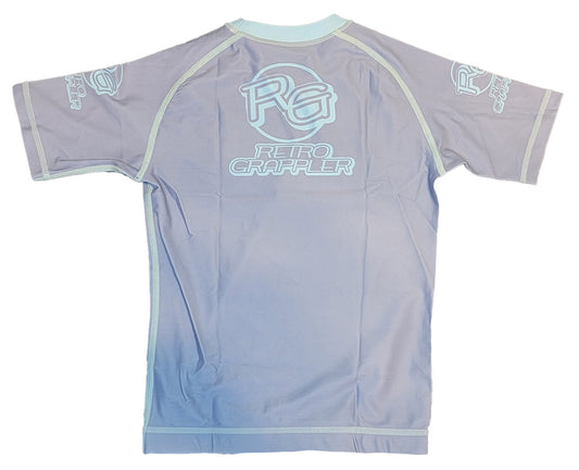 The Youth - Competition Shark by Retro Grappler is a light purple short-sleeve rash guard with white RG and Retro Grappler logos on the back and sleeves, light blue seam trim, four-way stretch fabric, and a fitted design shown laid flat (back view).