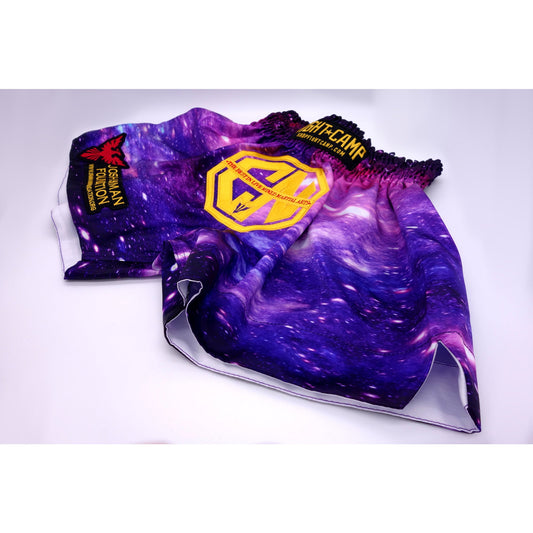 The Combat Night Galaxy Muay Thai shorts feature a purple galaxy pattern, yellow geometric logo, eagle patch, and FIGHT CAMP waistband—ideal for kickboxing fans. Displayed flat on a white surface. Brand: Combat Night.