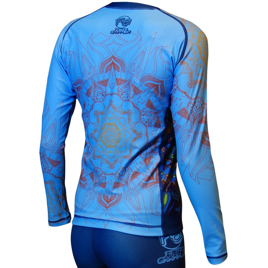 A person stands with their back to the camera, wearing the Retro Grappler Youth - Zen Line: Mandala Rash Guard, a fitted long-sleeve blue athletic top featuring intricate mandala and floral patterns on the back.