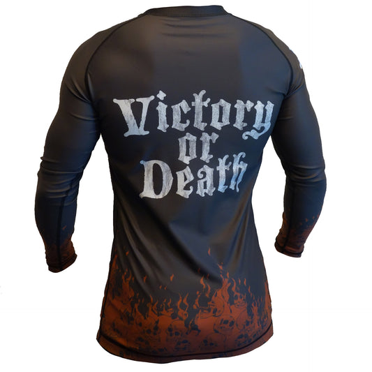 A person wearing a black Youth - Death Before Submission rashguard by Retro Grappler, featuring bold white Victory or Death text on the back and orange flaming skulls along the bottom hem.