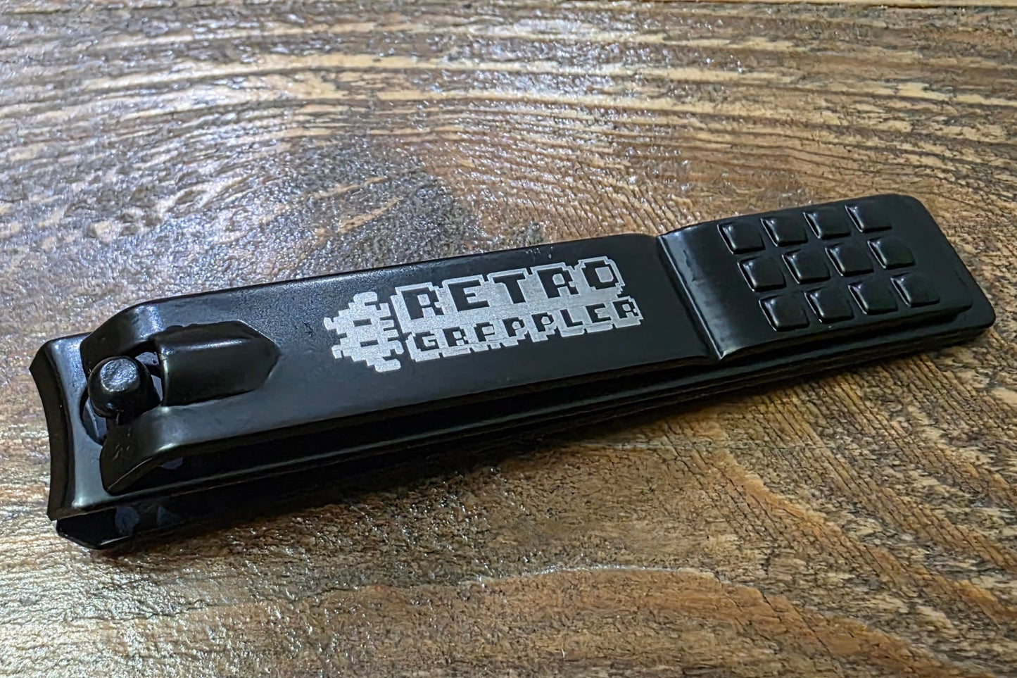 Black nail clipper with 'Retro Grappler' branding on a wooden surface